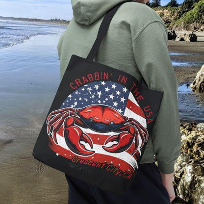 A black tote bag with an American Flag design with a crab coming out and says Crabbin' in the USA and Crescent City, CA.  