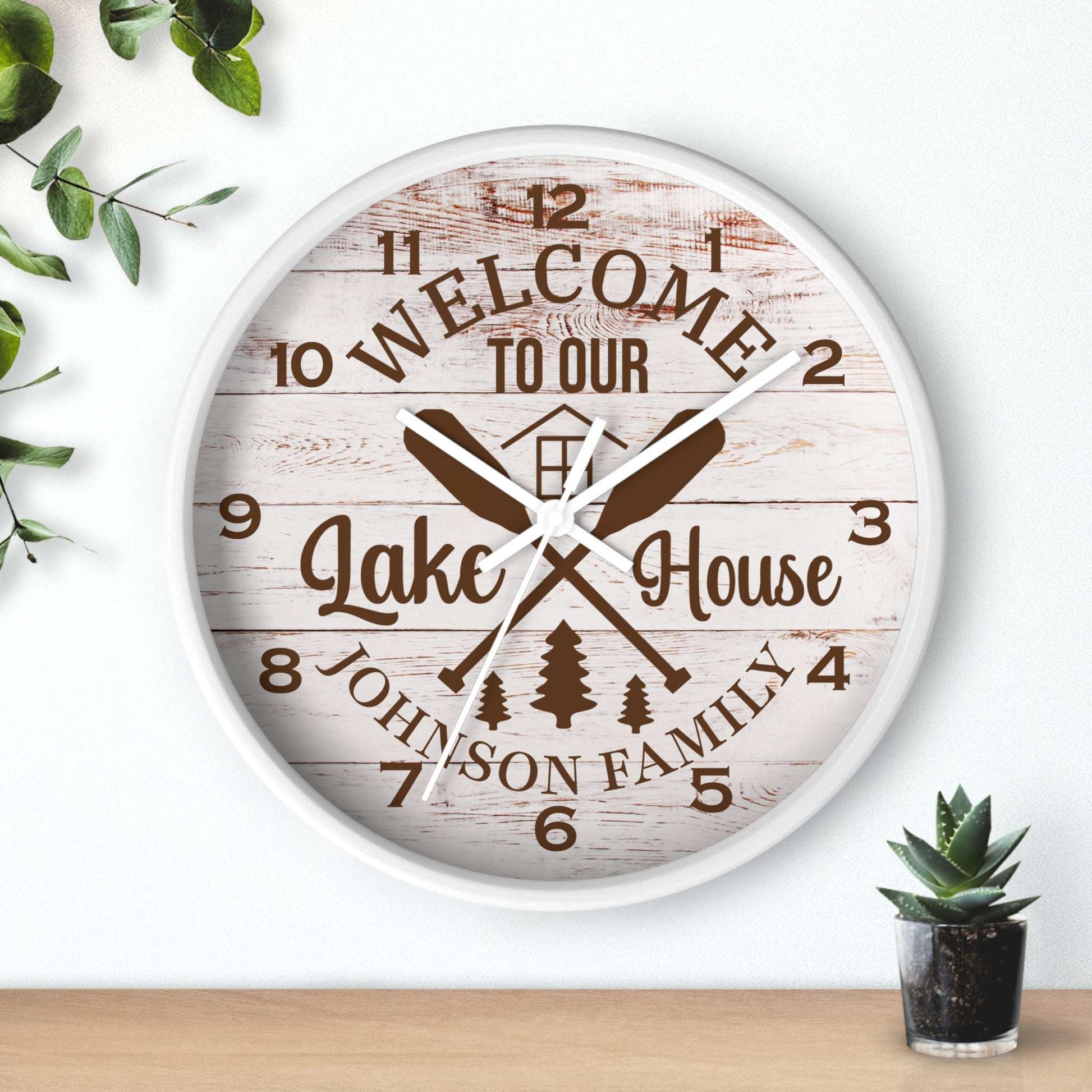 Wall clock with 'Welcome to our Lake House' text and oar design on a wooden background.