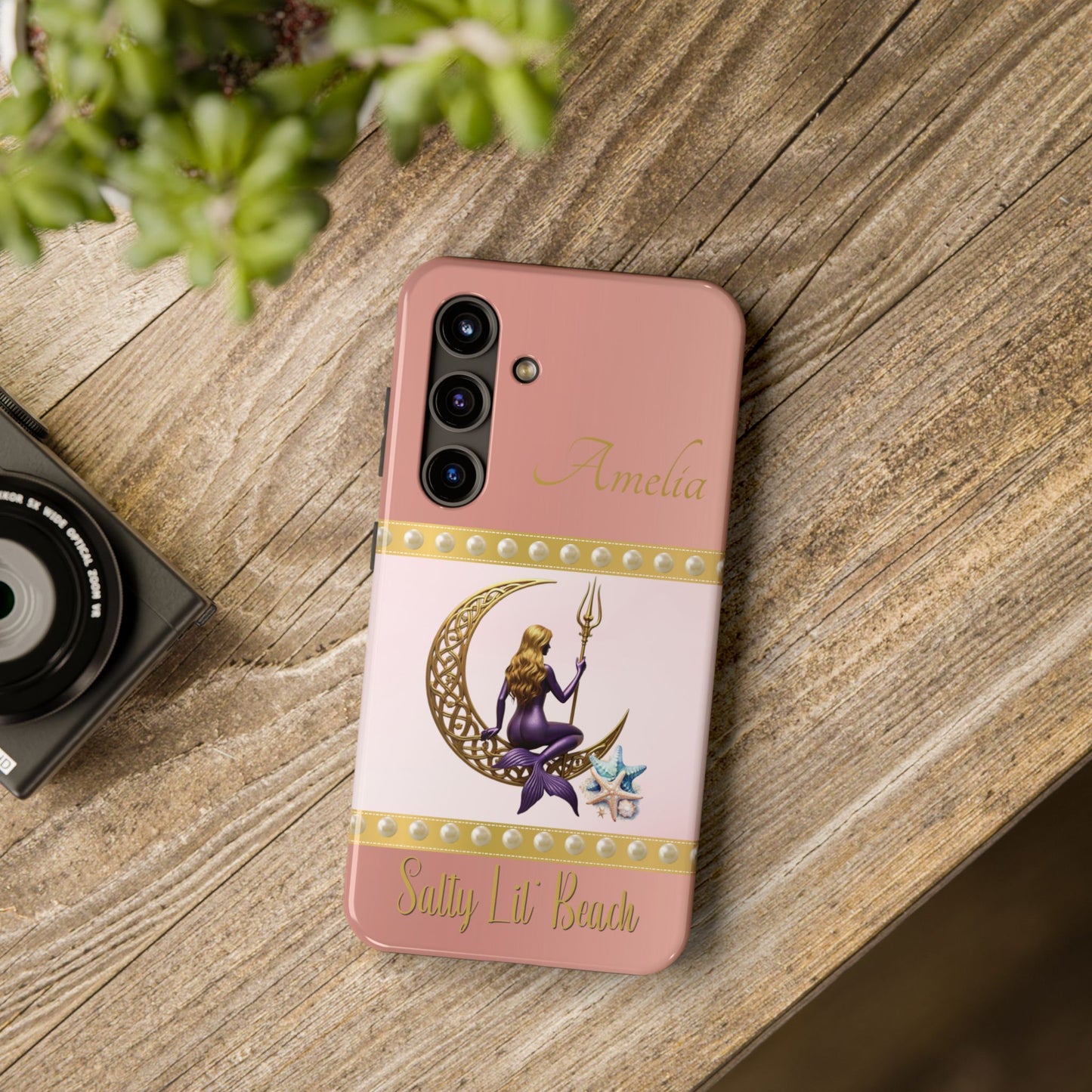 Phone case with mermaid design on a wooden surface next to a camera