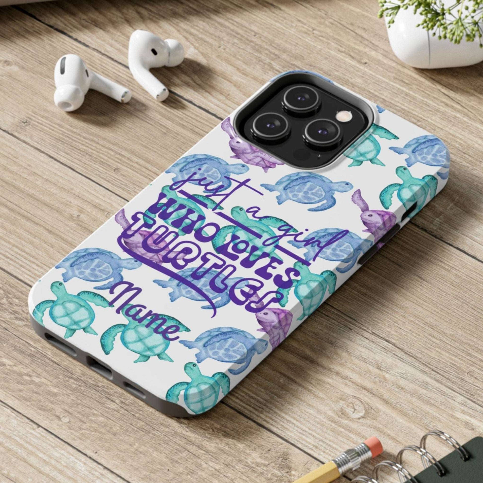 Phone case with turtle design on a wooden surface with laptop, earbuds, and notebook.