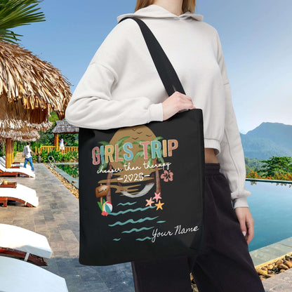 Person holding a black 20" x 20" tote bag with 'Girls Trip' beach design that can be personalized.