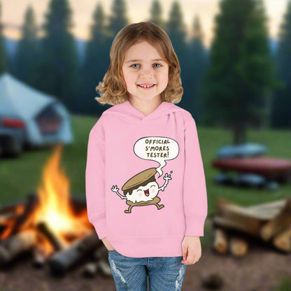 Girl wearing pink cozy toddler hoodie with “Official S’mores Tester” speech bubble and a cartoon s'more  – cute outdoor-themed sweatshirt for little campers.