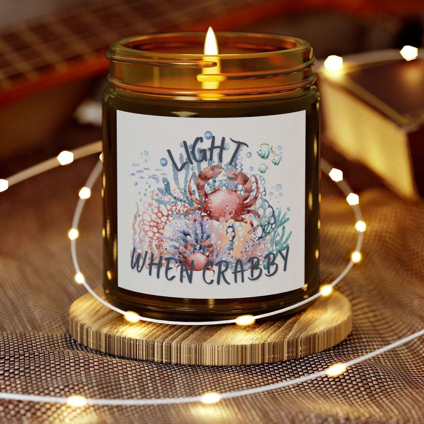 Candle in a jar with a decorative label on a wooden coaster, surrounded by string lights and a guitar in the background.