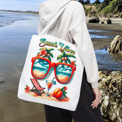 White 18" x 18" Tote bag featuring sunglasses with ocean and beach scene reflections, palm trees coming out of the glasses, a beach chair and cocktail on the sand, with the phrase "Beach Vibes" in a retro rainbow gradient font.