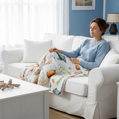 Woman sitting on a white couch with a white beach themed blanket with seashells in a cozy living room.
