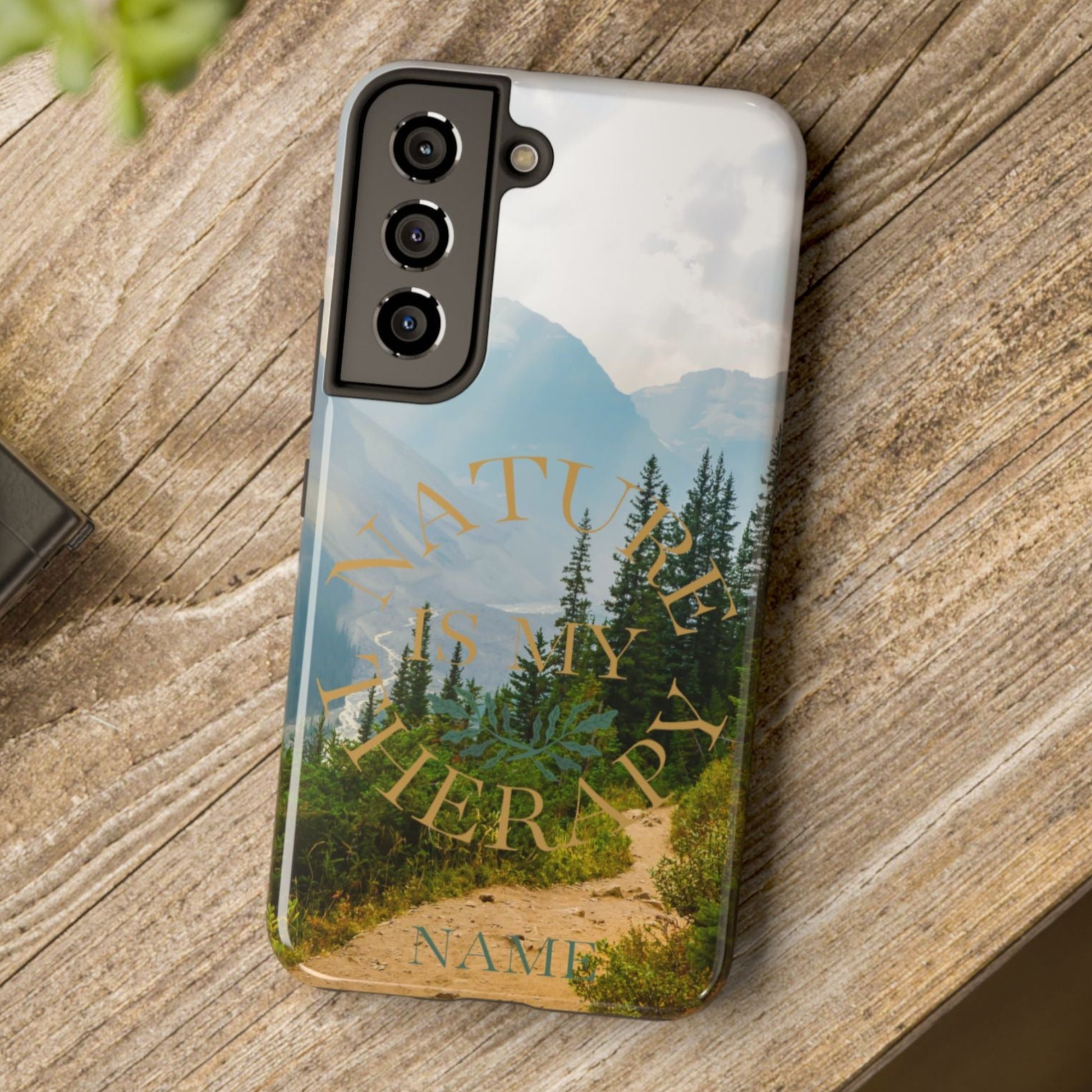 Phone case with nature design and 'Nature is my therapy' text on a wooden surface with a camera and plant.