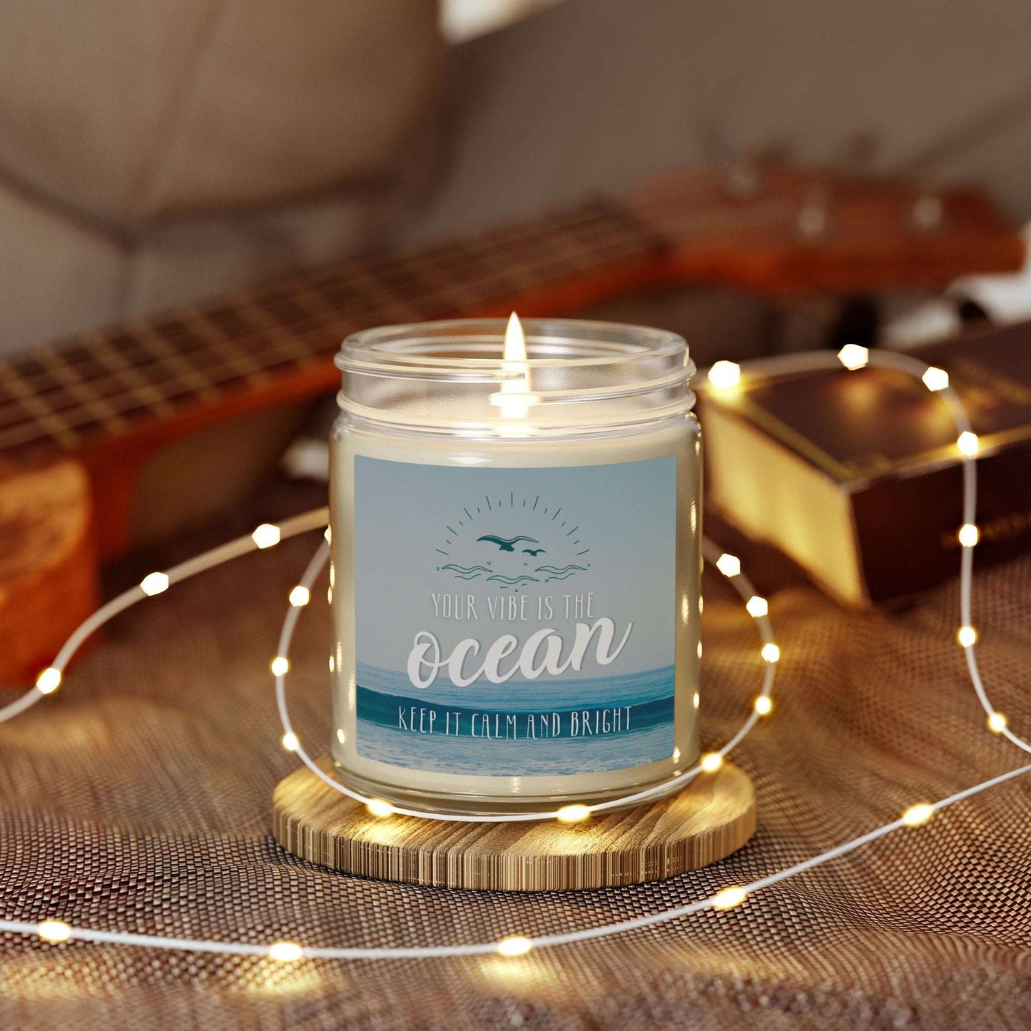Candle in a jar with a label on a wooden coaster surrounded by string lights and a guitar in the background