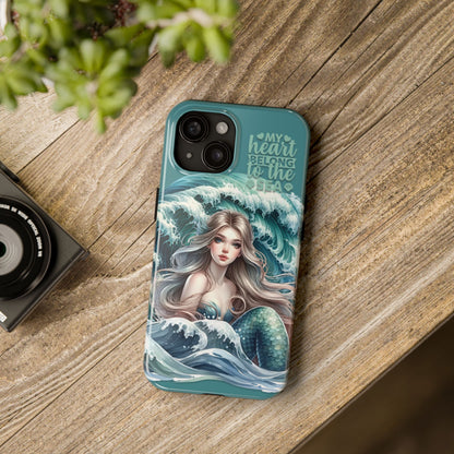 Phone Case with Flowy mermaid with ocean wave behind and text My Heart Belongs to the Sea laying on table