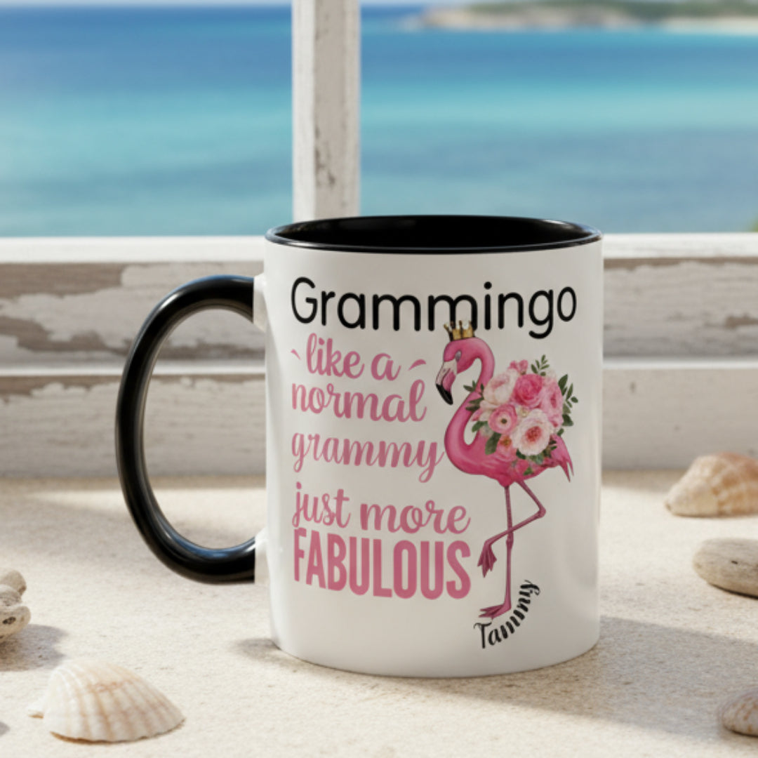 Ceramic coffee mug featuring a flamingo adorned with flowers and the text “Grammingo like a normal Grammy just more fabulous,” available with white, pink, or black handle options.