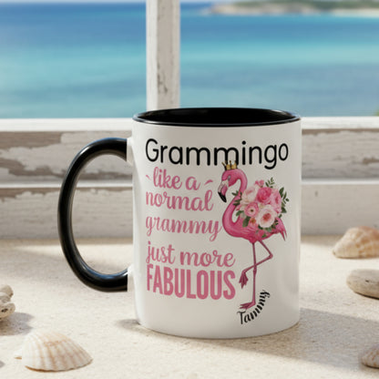 Ceramic coffee mug featuring a flamingo adorned with flowers and the text “Grammingo like a normal Grammy just more fabulous,” available with white, pink, or black handle options.