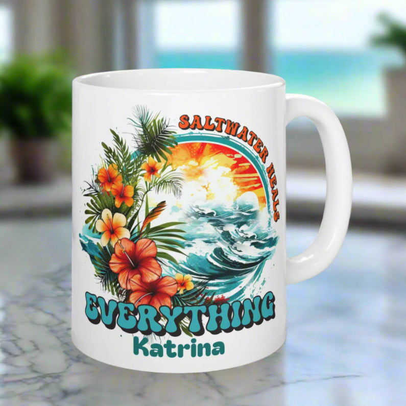 White mug with tropical design and text on a coaster, placed on a surface with a plant and container in the background.