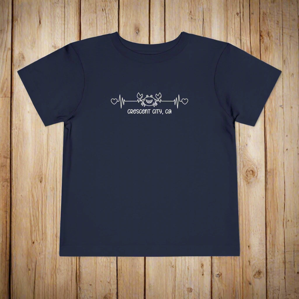 Navy Toddler t-shirt featuring a smiley crab on a heartbeat line with hearts at both ends and the text “Crescent City, CA” underneath.