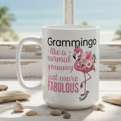 Ceramic coffee mug featuring a flamingo adorned with flowers and the text “Grammingo like a normal Grammy just more fabulous,” available with white, pink, or black handle options.
