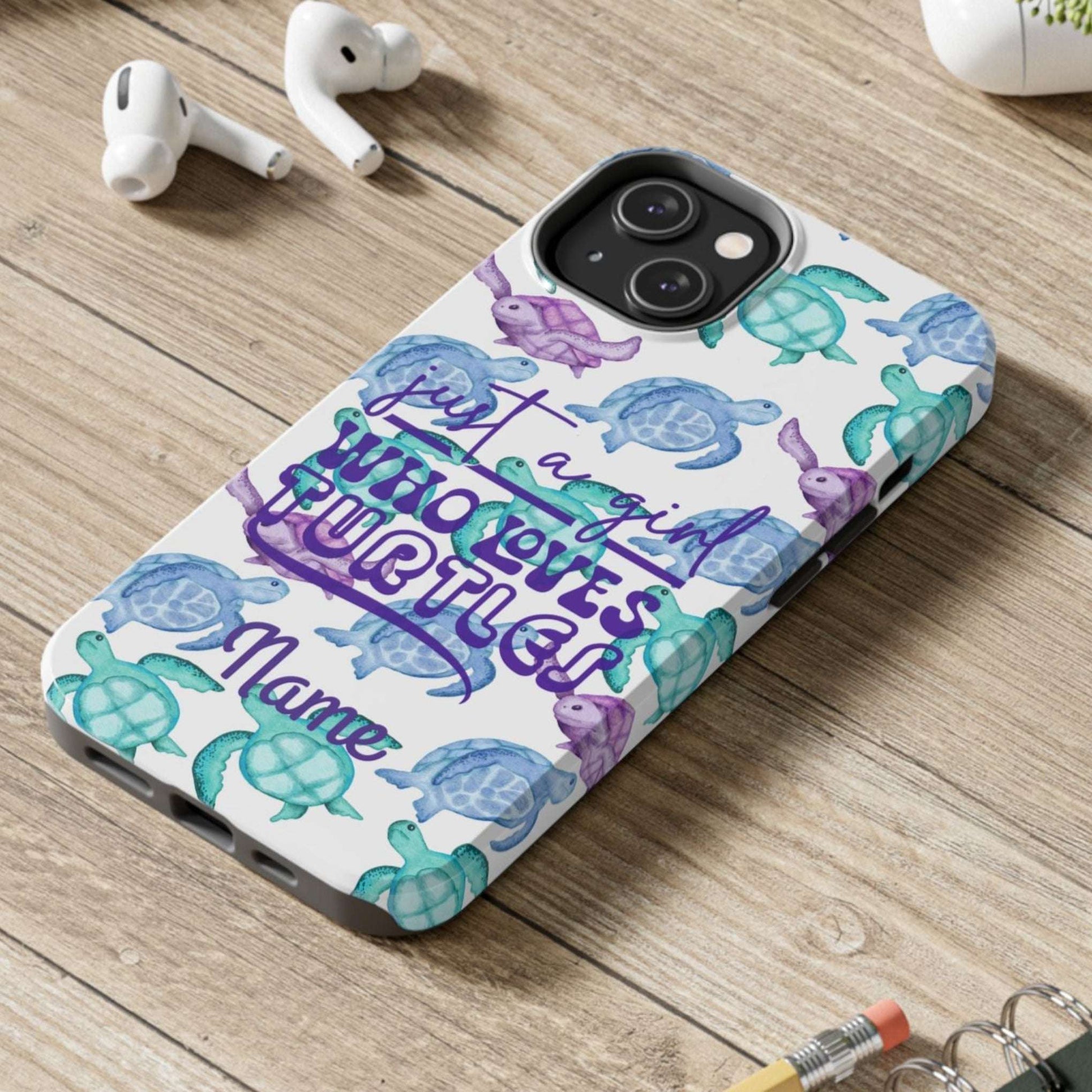 Phone case with sea turtle design and text on a wooden surface with laptop, earbuds, and notebook.