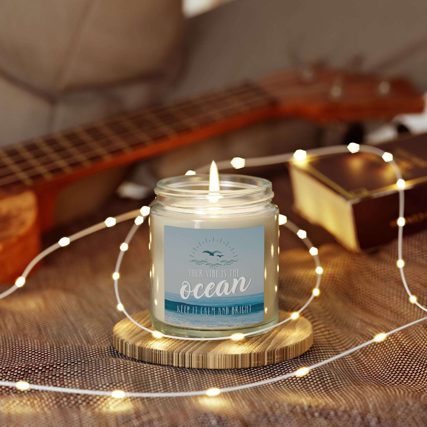 Candle in a jar labeled 'Ocean' with a guitar and string lights in the background