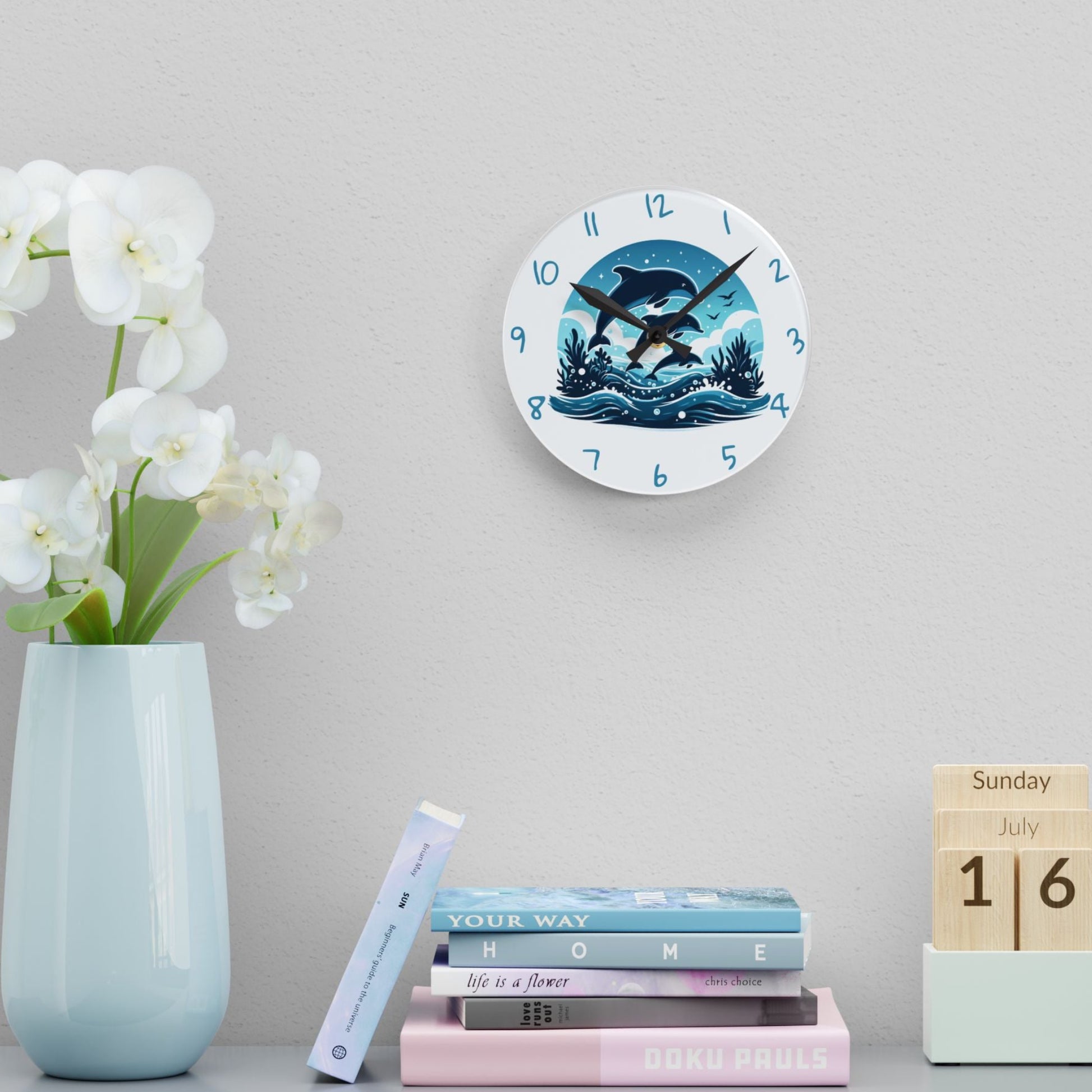 Decorative clock with swimming dolphins on a wall above books and a vase with flowers.