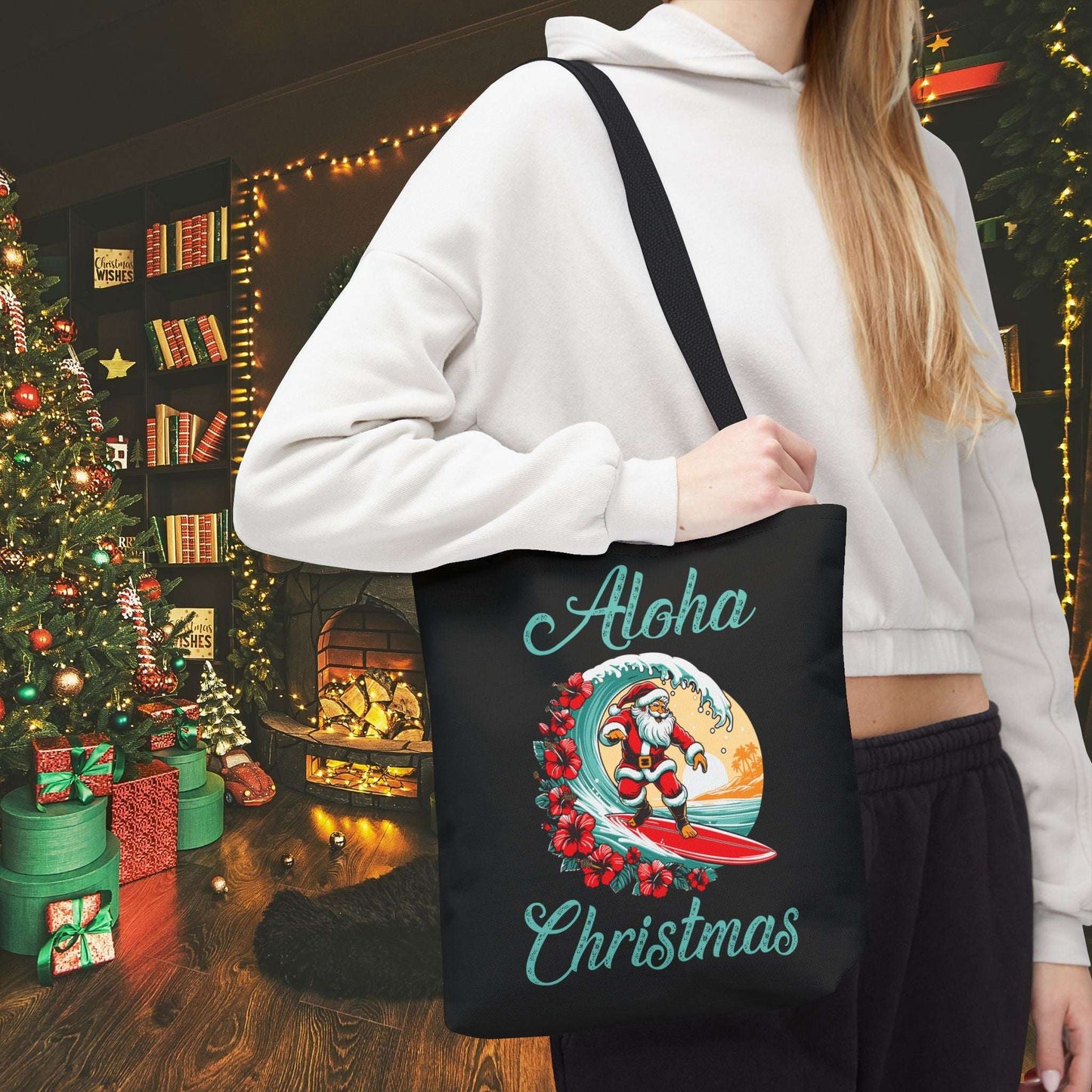 Person holding a black tote bag with 'Aloha Christmas' design in a festive indoor setting.