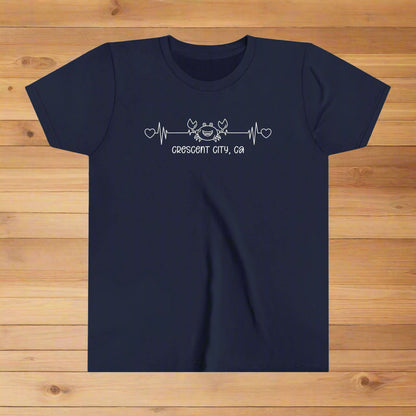Navy Youth t-shirt with a smiley crab on a heartbeat line with hearts at both ends and “Crescent City, CA” underneath the design.