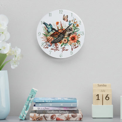 Decorative wall clock with floral and sea turtle design, placed on a shelf with books and a vase.