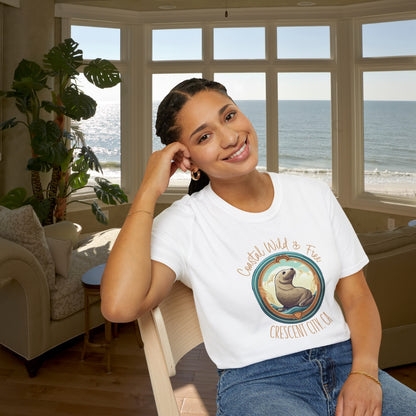 Woman wearing a white t-shirt with a graphic design sitting in a room with large windows overlooking the ocean.