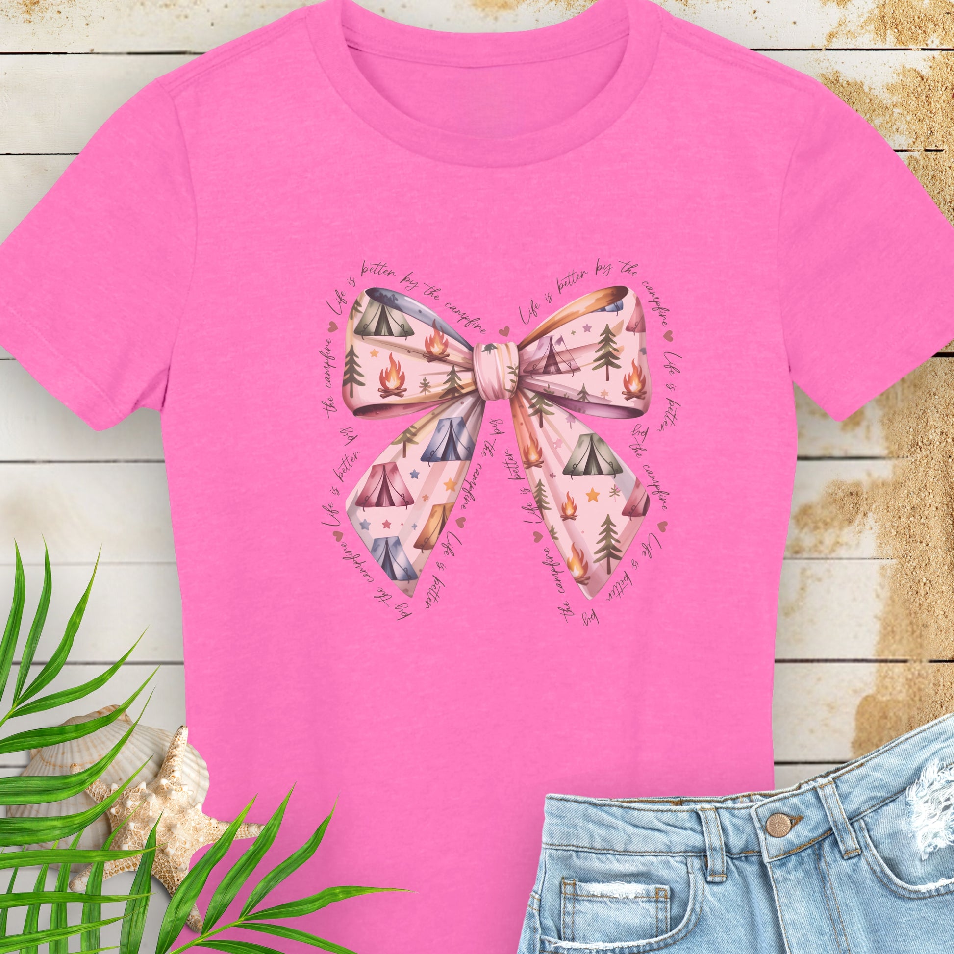 Pink t-shirt with a bow design on a wooden surface with leaves and jeans.