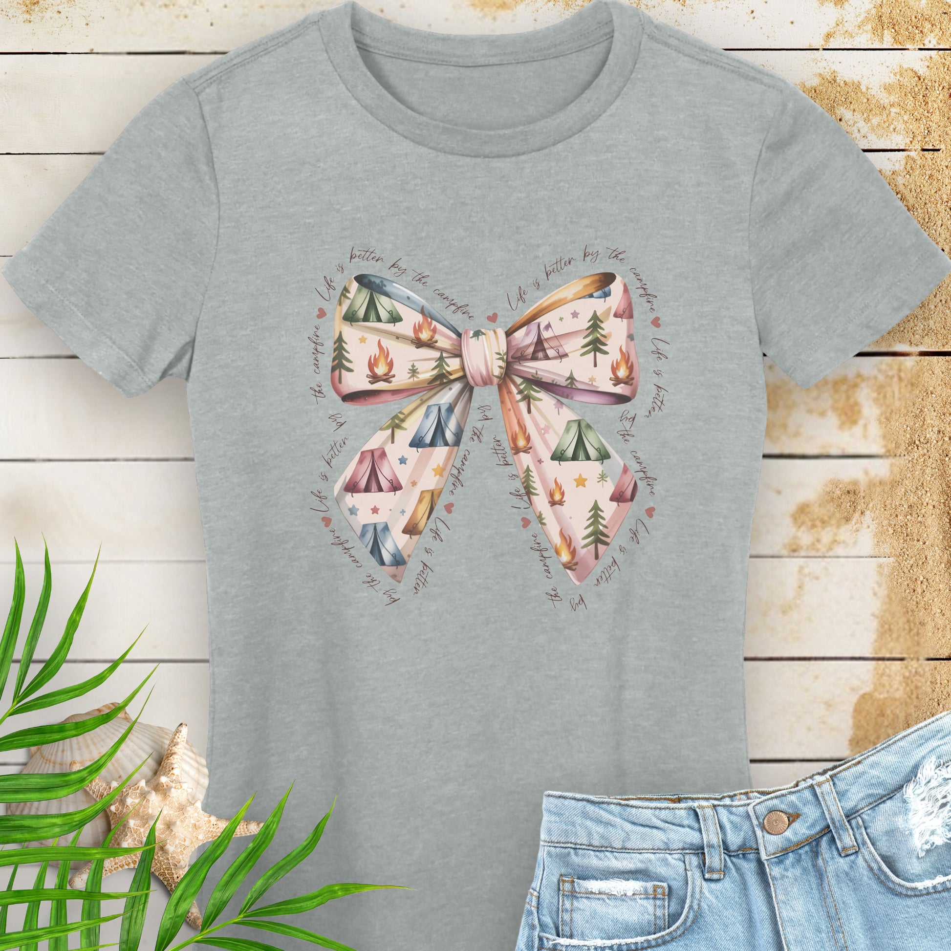Gray t-shirt with a bow and nature-themed design on a wooden surface with a plant and shell.