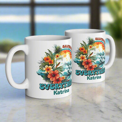 Two white mugs with tropical designs and text on a wooden surface.