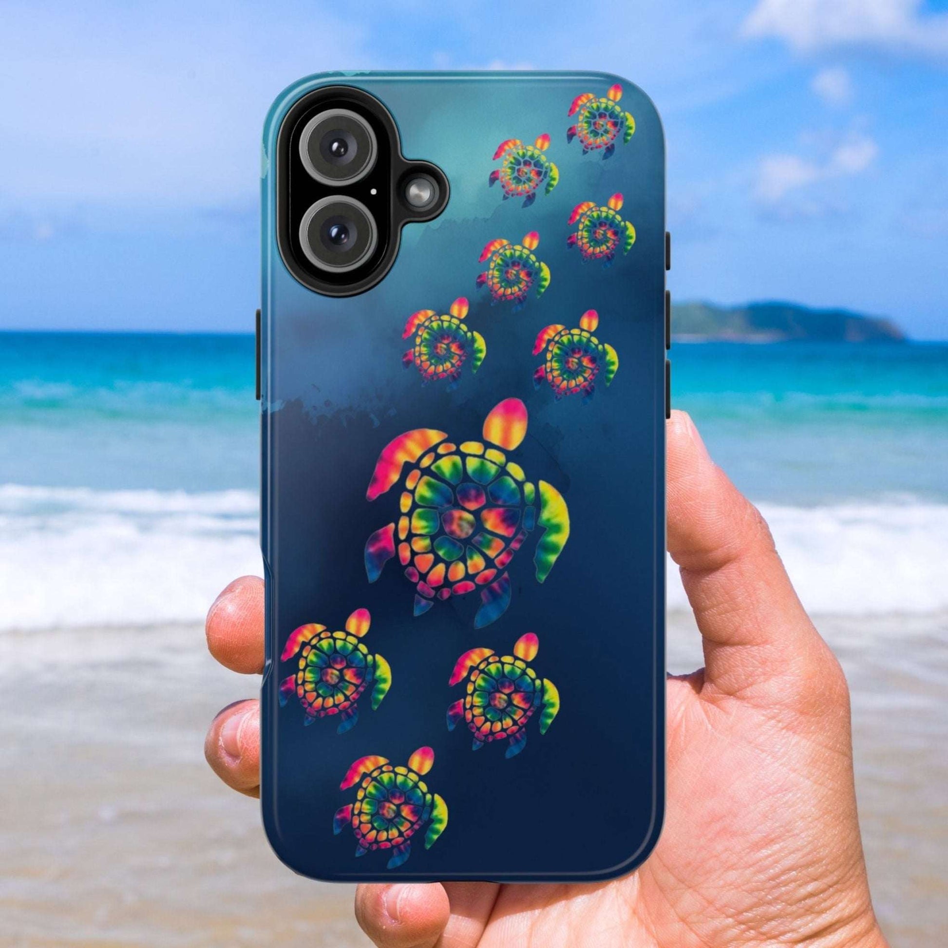 Phone case with colorful turtle design held by a hand on a beach