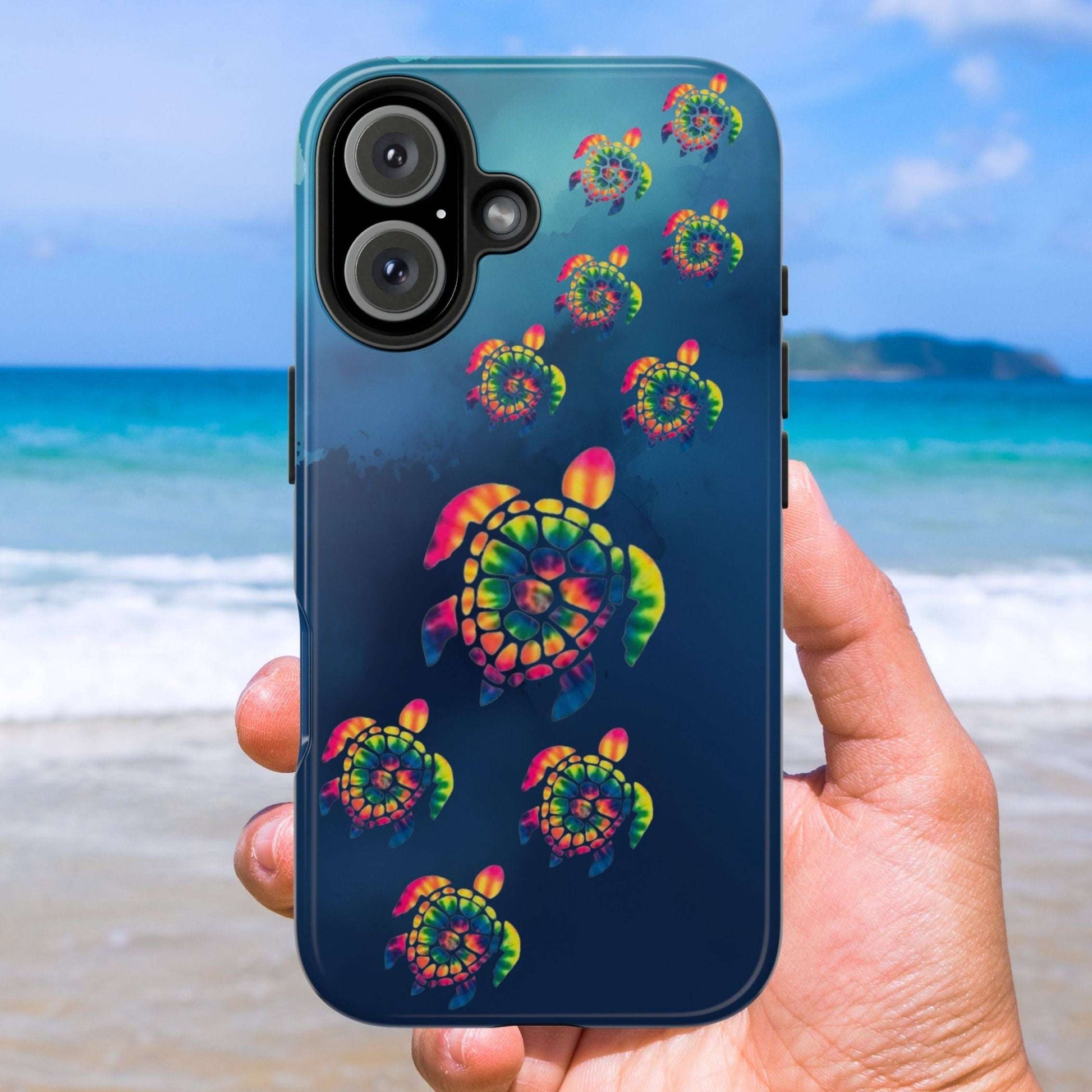 Phone case with colorful turtle design held by a hand on a beach