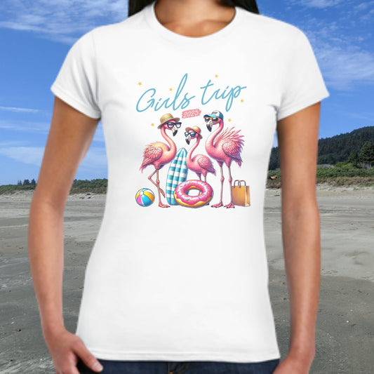 Person wearing a white t-shirt with flamingo design and 'Girls trip' text on a beach.