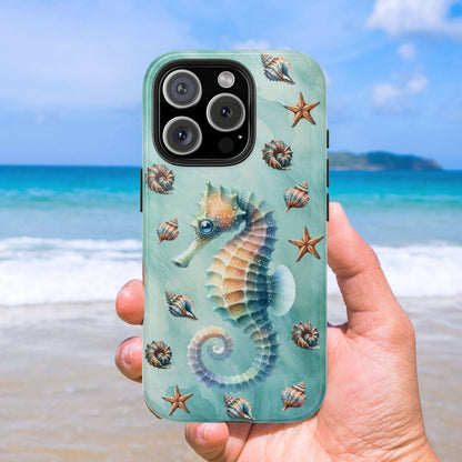 Phone case with seahorse and shell design held by a hand on a beach