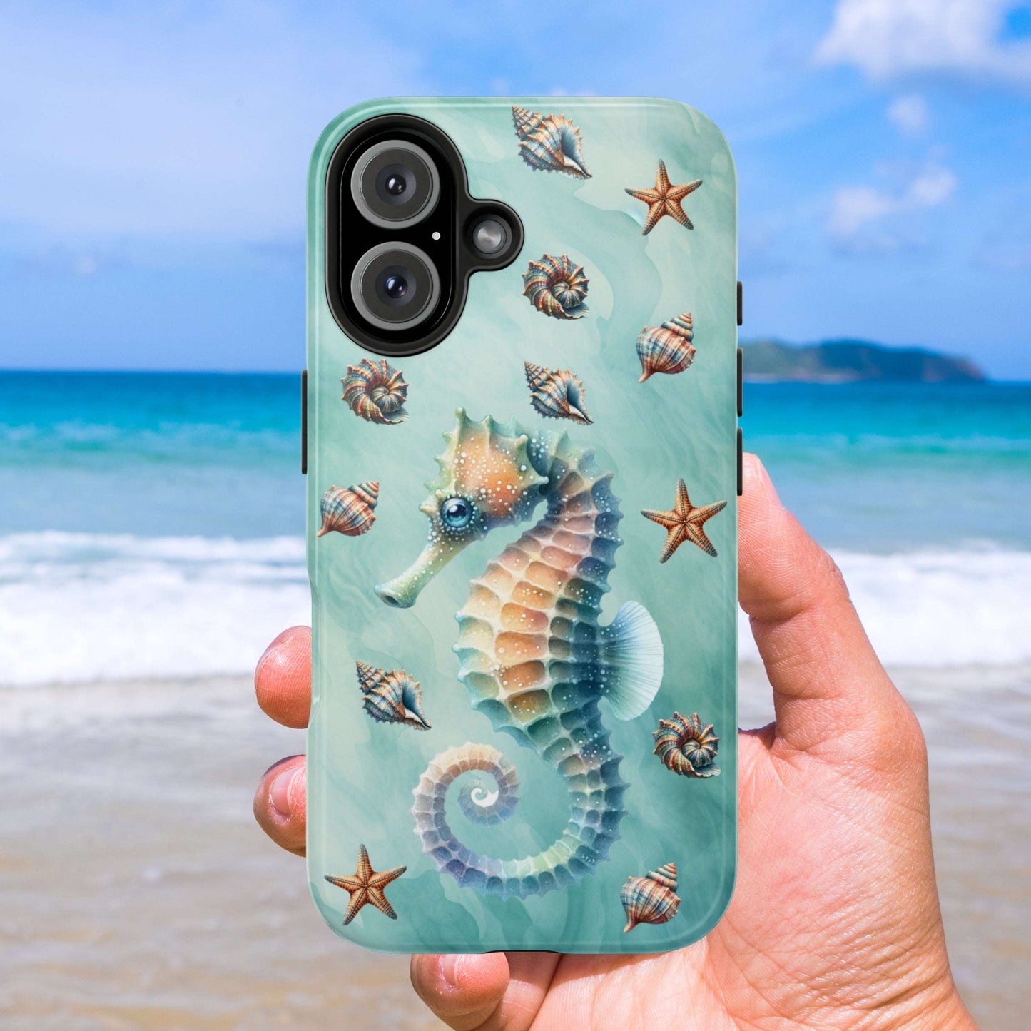 Phone case with seahorse and shell design held against a beach background