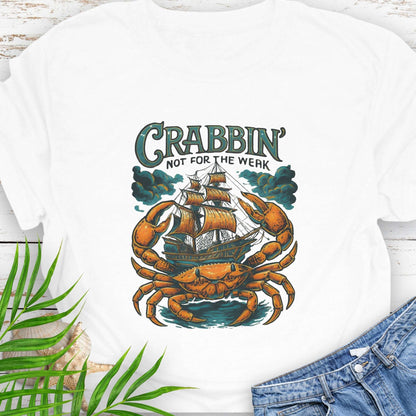 White t-shirt with a large crab enveloping a pirate ship with the text “Crabbin’s Not for the Weak” in an old-style font.