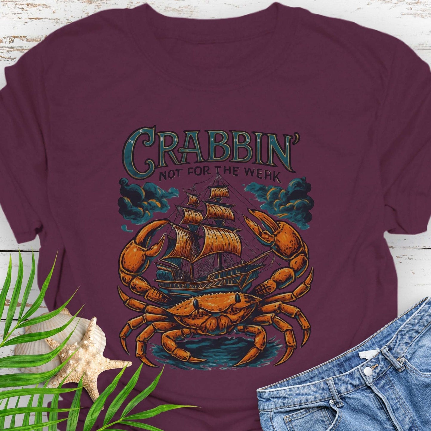 Maroon t-shirt with a large crab enveloping a pirate ship with the text “Crabbin’s Not for the Weak” in an old-style font.