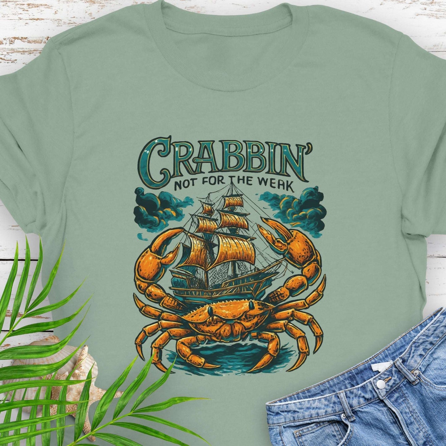 Green t-shirt with a large crab enveloping a pirate ship with the text “Crabbin’s Not for the Weak” in an old-style font.