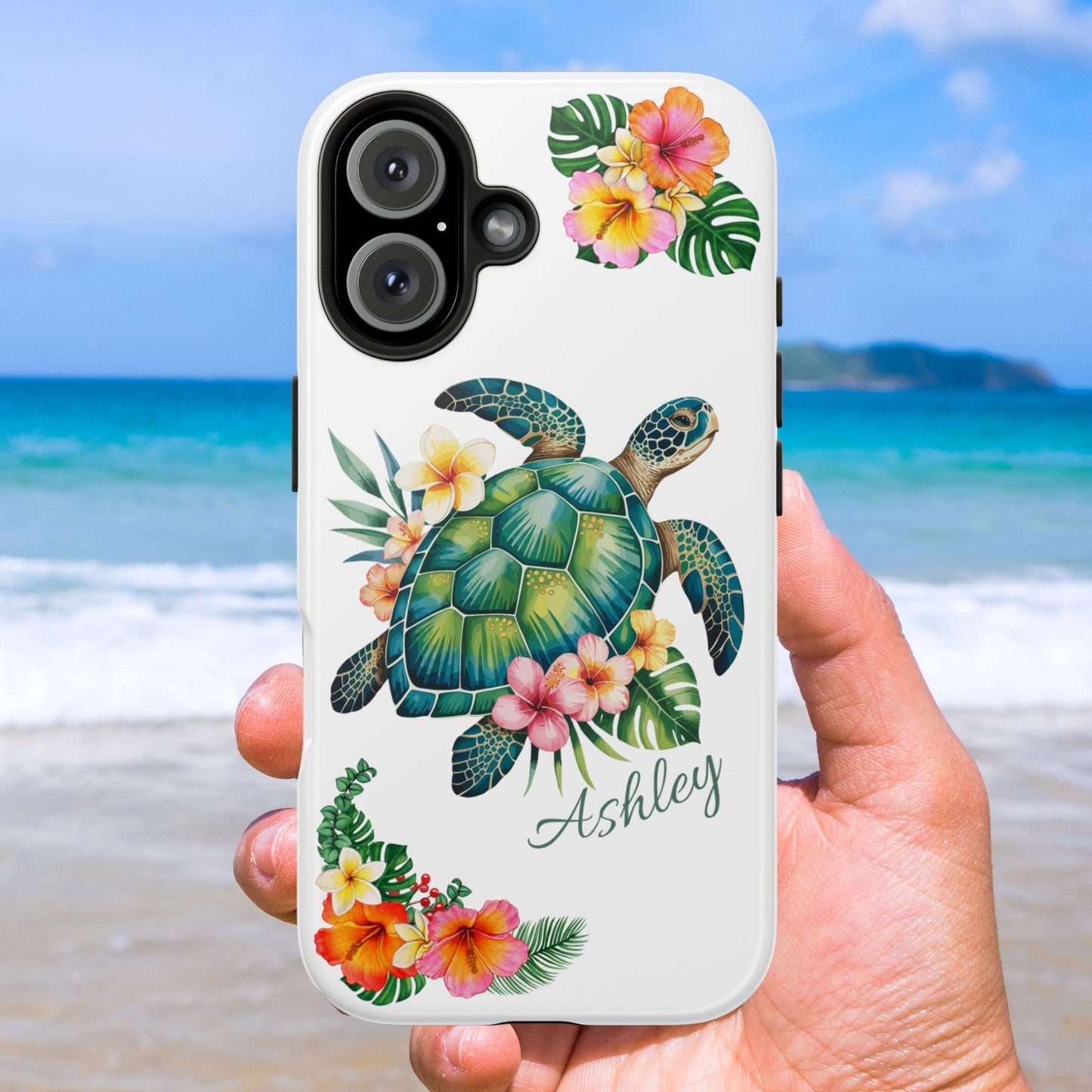 Phone case with a turtle design and floral elements held against a beach background