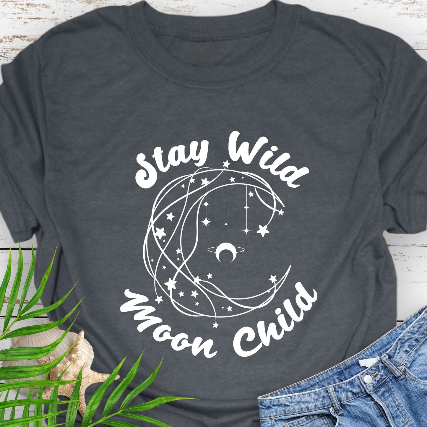 Dark gray T-shirt with crescent shaped lines and hanging crescent moon and stars that says Stay Wild Moon Child.