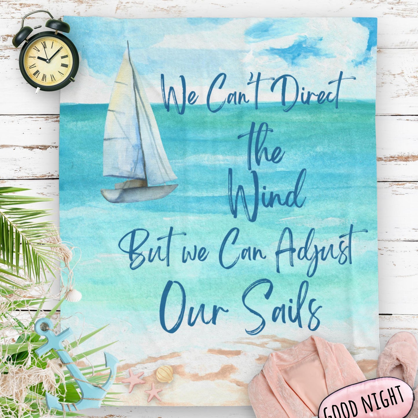 Blanket with ocean scene with sailboat sailing from coast with slogan "We Can't Direct the Wind But we Can Adjust Our Sails".