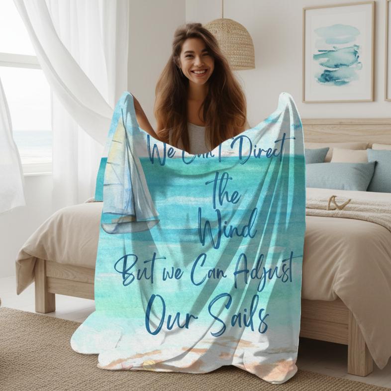 Woman holding 60" x 80" Blanket with ocean scene with sailboat sailing from coast with slogan "We Can't Direct the Wind But we Can Adjust Our Sails".