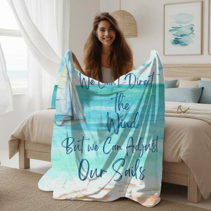 Woman holding 60" x 80" Blanket with ocean scene with sailboat sailing from coast with slogan "We Can't Direct the Wind But we Can Adjust Our Sails".