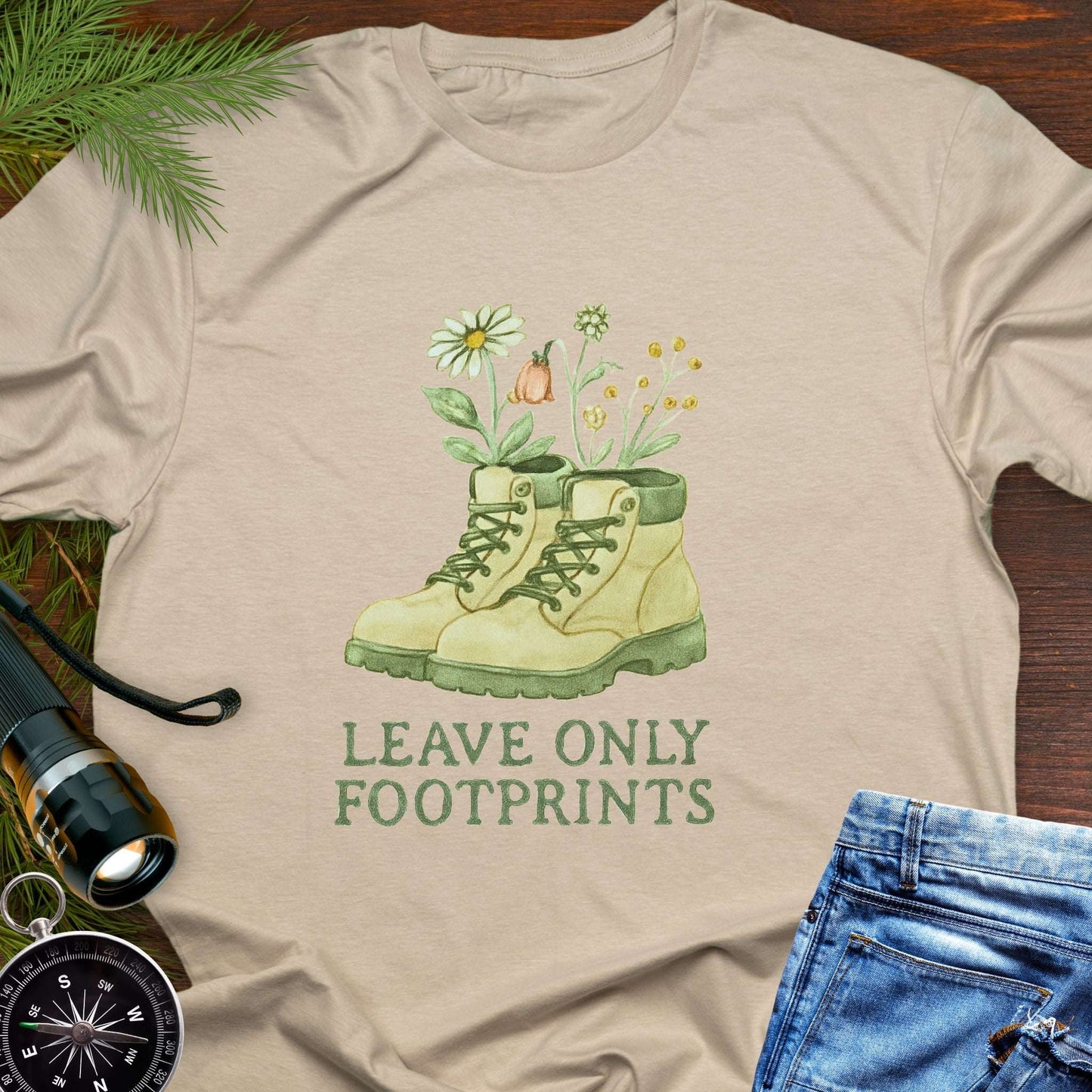 Beige T-shirt with hiking boots and wildflowers that says "Leave Only Footprints."
