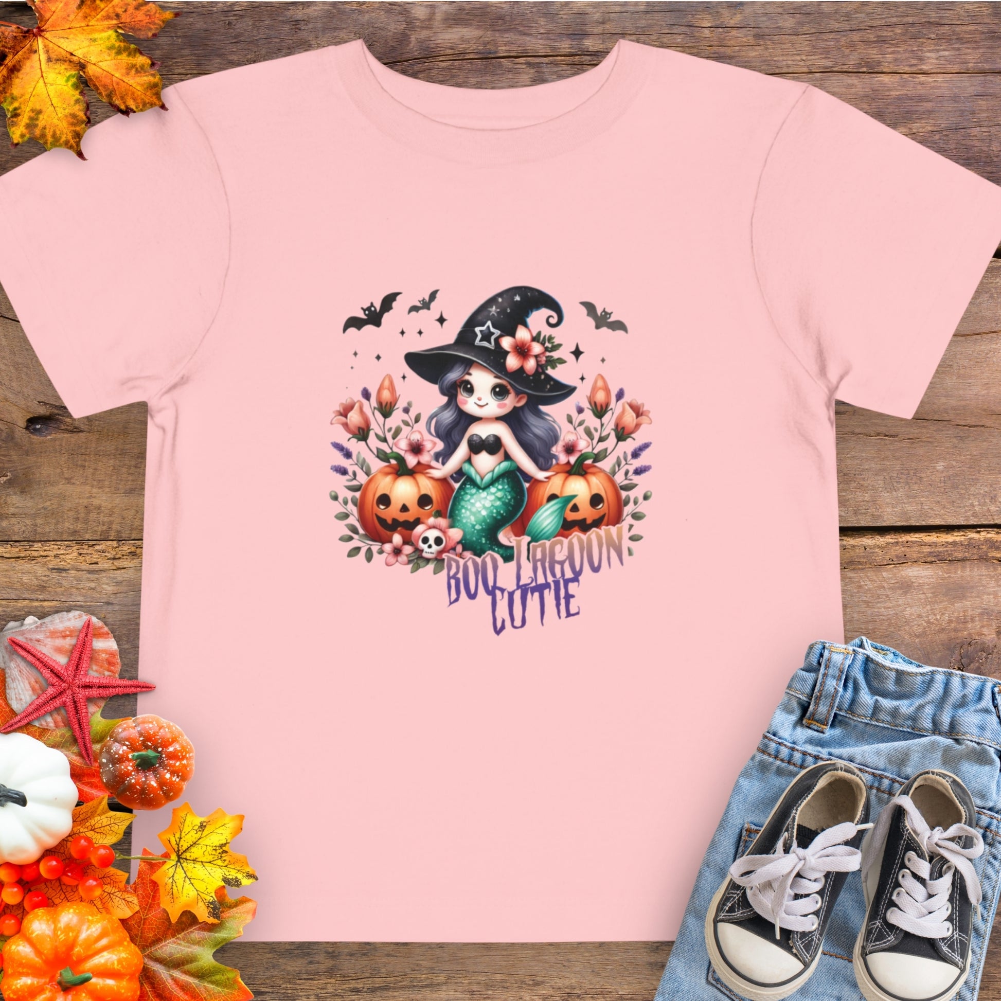 Pink Toddler t-shirt design with a witchy mermaid sitting among pumpkins and flowers, with bats flying overhead and the words “Boo Lagoon Cutie.