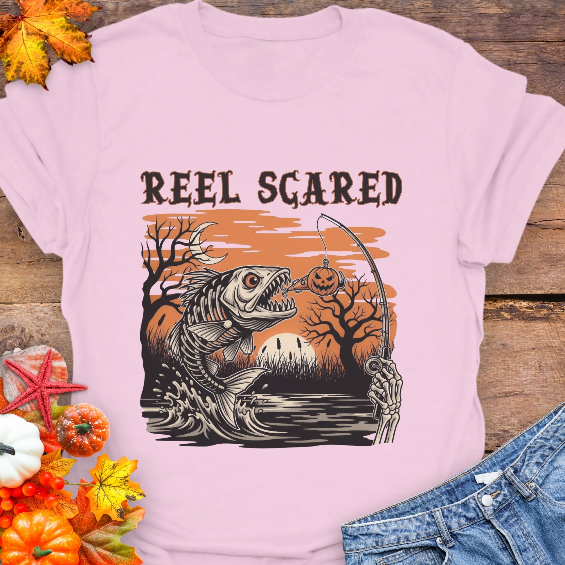 Pink t-shirt with a skeleton fish going for a hook and the phrase “Reel Scared.