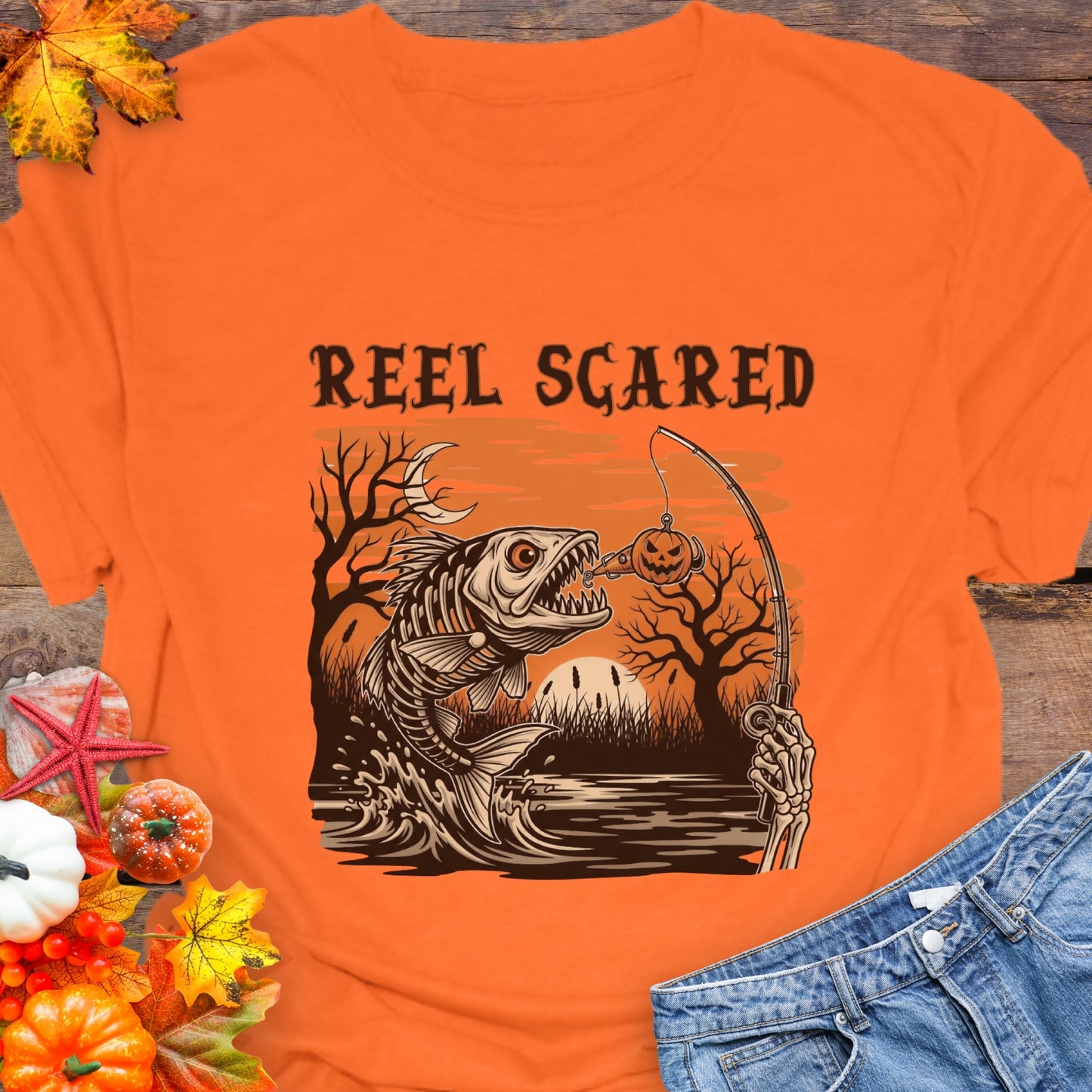 Orange t-shirt with a skeleton fish going for a hook and the phrase “Reel Scared.