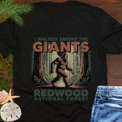 Black t-shirt with Bigfoot graphic and text 'I walked among the giants Redwood National Forest' on a wooden surface.