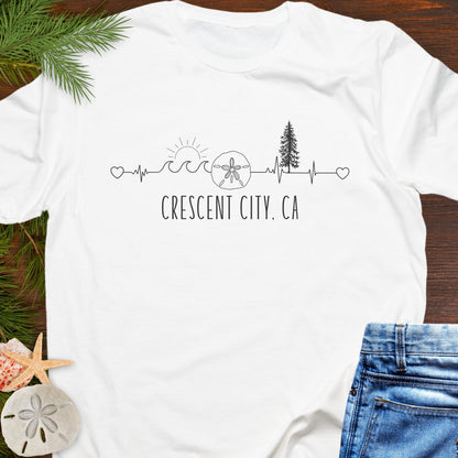 White t-shirt with white heartline with redwoods, waves, and sand dollar with text 'Crescent City, CA'.