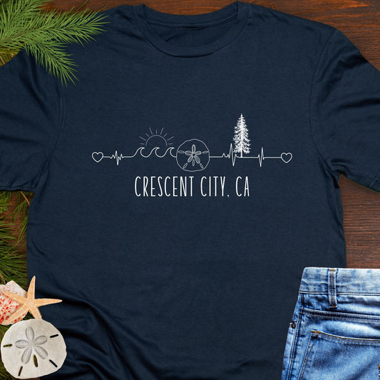 Navy blue t-shirt with white heartline with redwoods, waves, and sand dollar with text 'Crescent City, CA'.