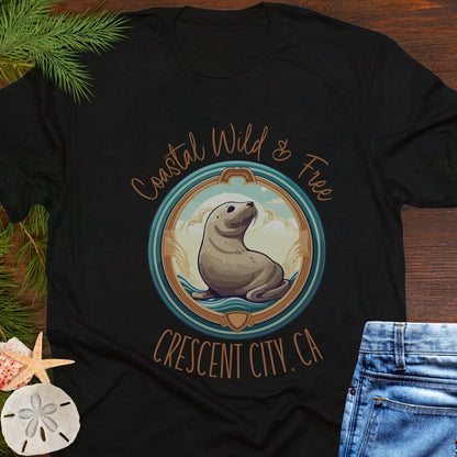 Black t-shirt with a seal graphic and text on a wooden surface with beach-themed items.