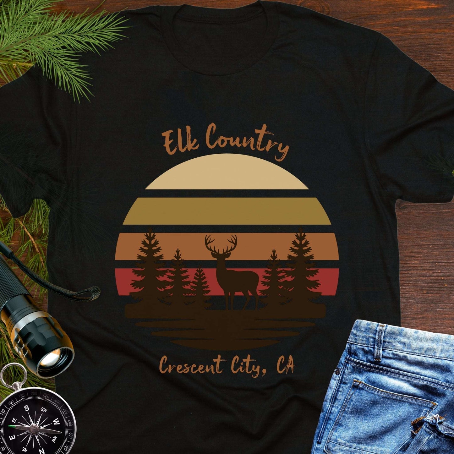 Black t-shirt with muted retro sunset with brown silhouette deer and trees with text 'Elk country Crescent City, CA.