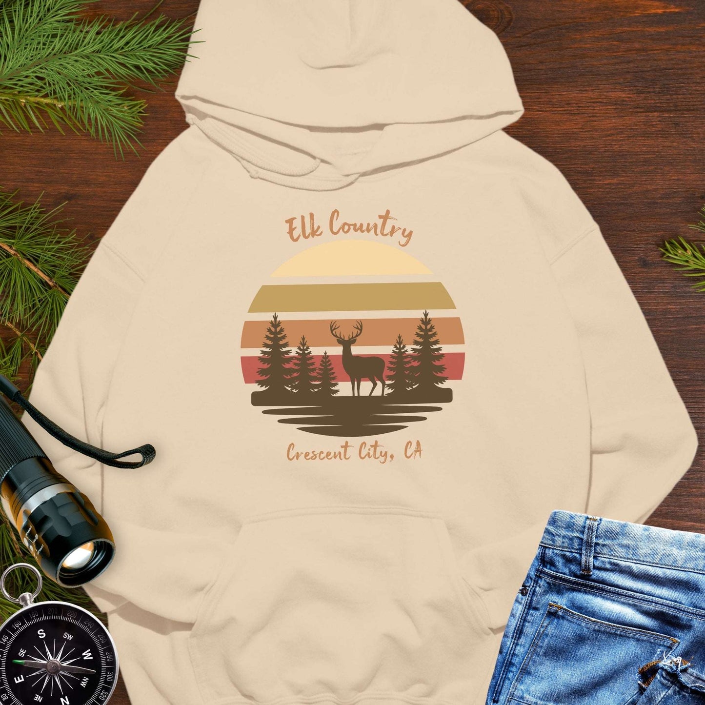Beige hoodie with 'Elk Country' with retro sunset and silhouette of trees and elk design with Crescent City, CA underneath.